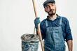 A man in a blue overalls holding a bucket and a pole