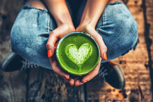 Sitting Woman Holding Cup With Green Matcha Latte. Matcha Latte With Heart Art Design.