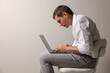 Man with bad posture using laptop while sitting on chair against grey background. Space for text