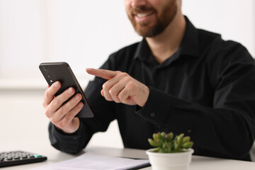 Poster - Smiling man using smartphone at table in office, closeup