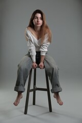 Poster - Beautiful young woman sitting on stool against grey background