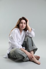 Poster - Portrait of beautiful young woman sitting on grey background