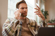 Portrait of confused man arguing with someone over the phone, businessman discuss project, looking at chart on laptop screen, using mobile phone to make a call, staring at monitor with frustration