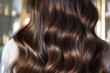 A woman with long brown hair, styled in soft waves and curls.