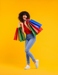 Wall Mural - Happy young woman with shopping bags on yellow background