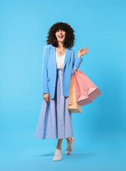 Wall Mural - Happy young woman with shopping bags on light blue background. Space for text