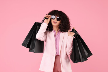 Wall Mural - Happy young woman with shopping bags and stylish sunglasses on pink background