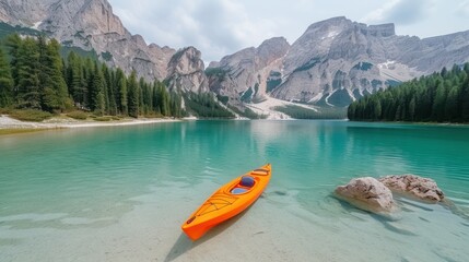 an orange kayak sitting on the shore of a lake in front of a mountain range with pine trees in the foreground.