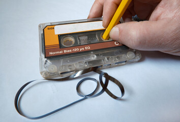 Vintage audio cassette and rewinding the magnetic data carrier with wooden pencil.