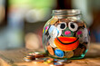 A child's piggy bank. A transparent glass jar filled to the brim with coins