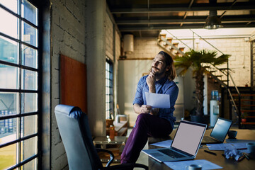 Wall Mural - Businessman with documents sitting on desk with laptops in modern loft office