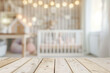 Blurred children's room with a wooden table top and baby crib in the background, space for product display or montage of your products. Background with bokeh lights for decoration, interior design.