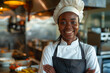 Smiling African Female Chef in Chef's Hat and Apron Stands Proudly in Restaurant Kitchen with Arms Crossed