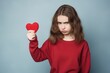 Young girl showing displeasure while holding a red heart, expressing a concept of heartbreak or disappointment. Unhappy Girl Holding Red Heart with Sad Expression
