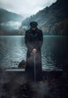 Vintage Elegance: Man with Cap and Black Coat Holding Sword by Lakeside