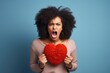Frustrated young woman yelling and holding a red heart-shaped pillow on a vivid blue background. Angry Woman Clutching Red Heart Pillow Against Blue