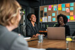 © Pillow Productions - During a business meeting, a group of professional women sit around a wooden table, smiling and laughing.