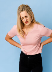 Portrait of a woman suffering, holding her aching lower back, she has a lumbago condition and her face is expressing pain, she needs to see a doctor, to take painkillers, to undergo X-rays and an MRI