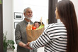© New Africa - Courier giving paper bag with food products to senior man indoors
