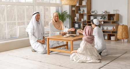 Wall Mural - Happy Muslim family sitting at table with traditional sweets in living room. Eid al-Fitr celebration