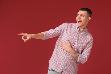 Sticker - Portrait of happy young man laughing and pointing at something on red background