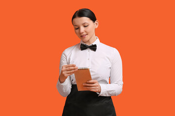 Wall Mural - Beautiful young waitress with notebook on orange background