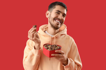 Wall Mural - Young man with heart-shaped chocolate candies on red background