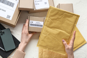 Poster - Female hands holding cardboard package with  label and envelopes at white table