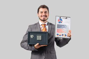 Wall Mural - Happy young man holding safe box and clipboard with graphics on grey background