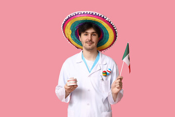 Wall Mural - Young male dentist with sombrero, jaw model, maracas and flag of Mexico on pink background