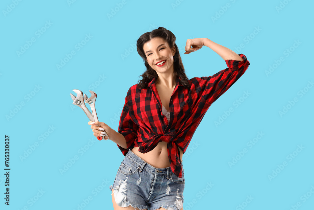 Beautiful pin-up woman with wrenches on color background