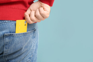 Poster - Young man putting credit card in jeans pocket on blue background, closeup