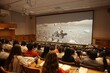 © Good Shot - A lecture hall with a large display showing a lunar rover, representing space exploration education.