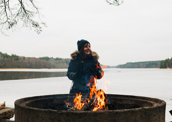 Wall Mural - woman stood warming her hands on the fire next to a Swedish lake