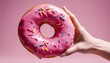 Pink donut being held up by a womens hand