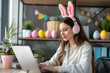 Work from home office easter concept with young woman using laptop and headphones in form of headband with rabbit ears.