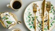 A set of porcelain coffee cups with gold metal decoration and green bird pattern, paired with gold cutlery to serve tea or coffee in an elegant way, all placed next to a white plate decorated 