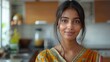 Self-assured, attractive Indian lady gazing at the camera in her kitchen at home. Joyful, stunning Hindu woman in her 20s, living in India, captured in a close-up headshot.