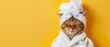 A ginger cat dressed in a cozy white bathrobe with a towel wrapped around its head, posing on a yellow background