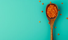 red lentils in a wooden spoon seen from above on a pastel blue / green background, top view banner with copy 

