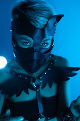 Sticker - portrait of a hot sexy girl in a leather cat mask and muzzled in bdsm handcuffs on neon blue light