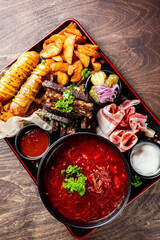 Wall Mural - A vibrant display of a hearty meal featuring grilled meat, assorted fried sides, fresh vegetables, and a bowl of red soup, showcasing a mix of textures and colors.