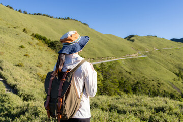 Poster - Girl on mountain peak with green grass looking at beautiful mountain valley