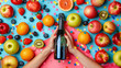 Colorful flat lay of fresh fruits with hands holding a bottle of sparkling drink on a blue background.