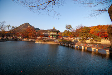 Wall Mural - Scenic autumn landscape with a lake, bridge, colorful trees, and mountains.