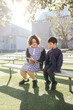 © Austockphoto - Two school students sitting outside on benches looking at a clipboard