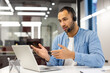 © Tetiana - A young Latin American man in a headset works in the office on a laptop, conducts an online consultation and business meeting, explains and gestures with his hands