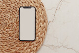 Fototapeta Konie - Smartphone with Blank screen on round rattan casket and beige marble background