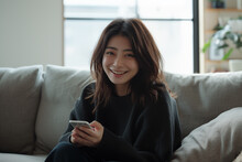 Radiant young Asian woman using smartphone on cozy sofa