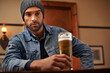 Beer, pub and male person thinking with alcohol, drinks and restaurant for entertainment. Pensive, lonely and bar for thoughtful or social for relax, night and beanie for cold weather in England
